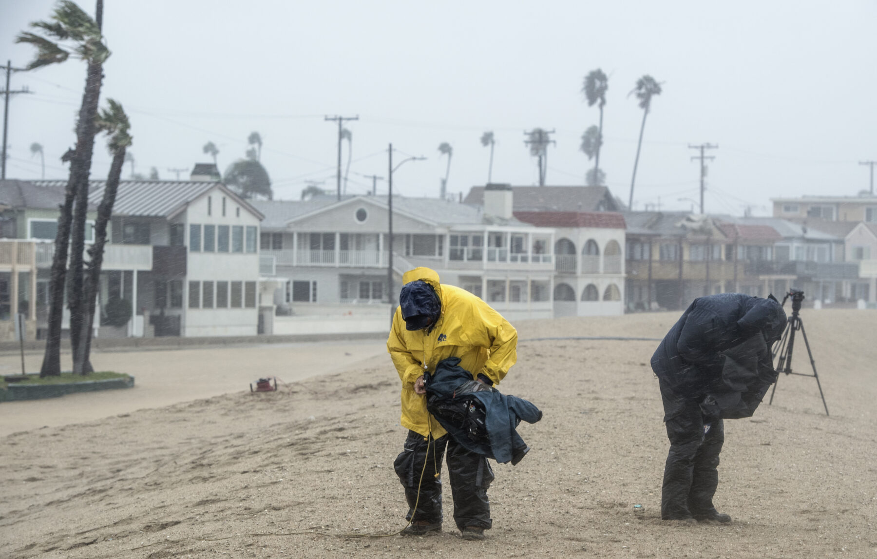 An NBC 4 news crew protects their gear during rain in Seal Beach, California in February 2017.